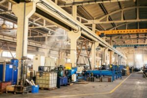 Operario utilizando un vehículo eléctrico industrial BKL Cargo para el transporte rápido de componentes en el pasillo de una planta de fabricación.